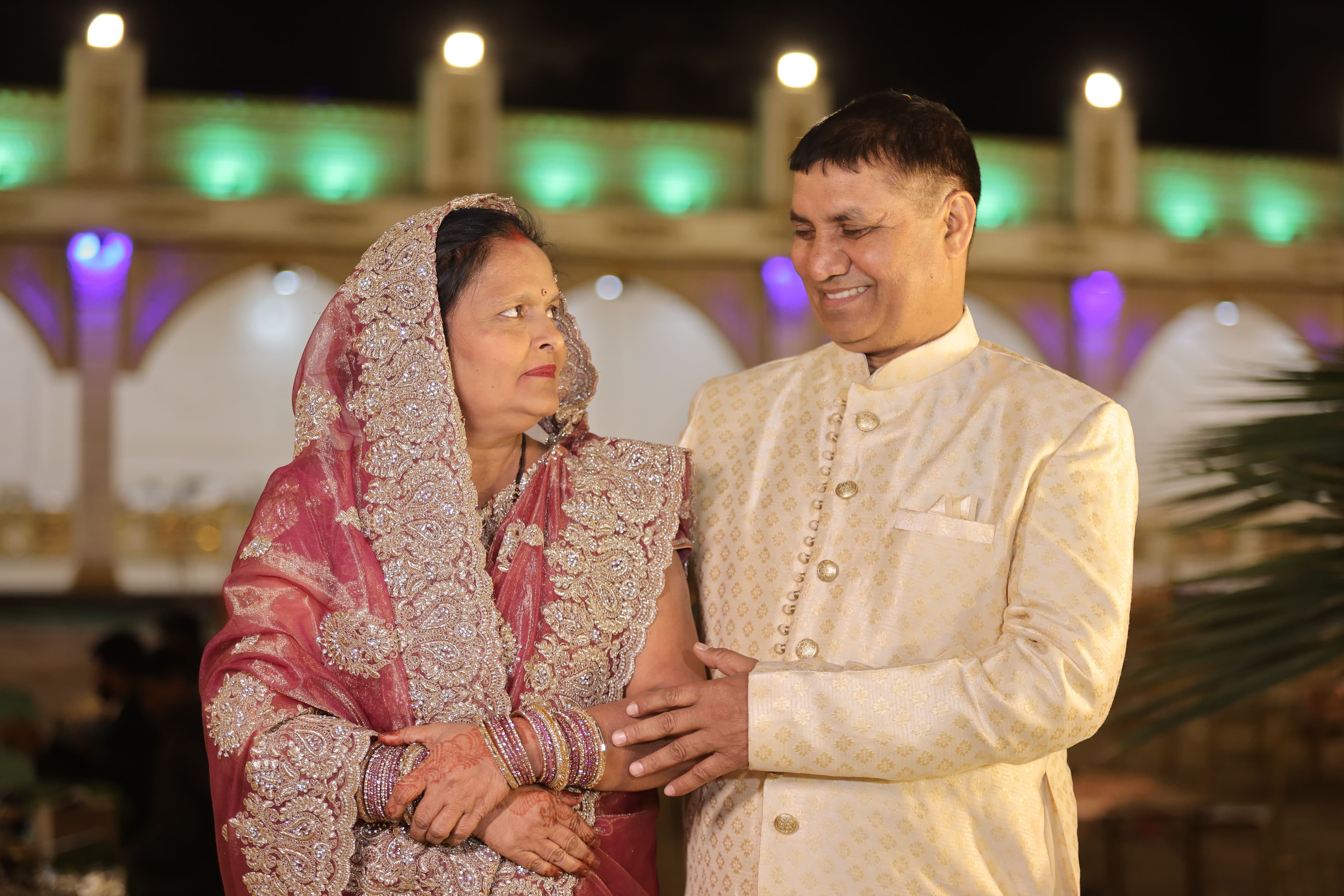 An elderly Indian couple dressed elegantly at a festive evening event