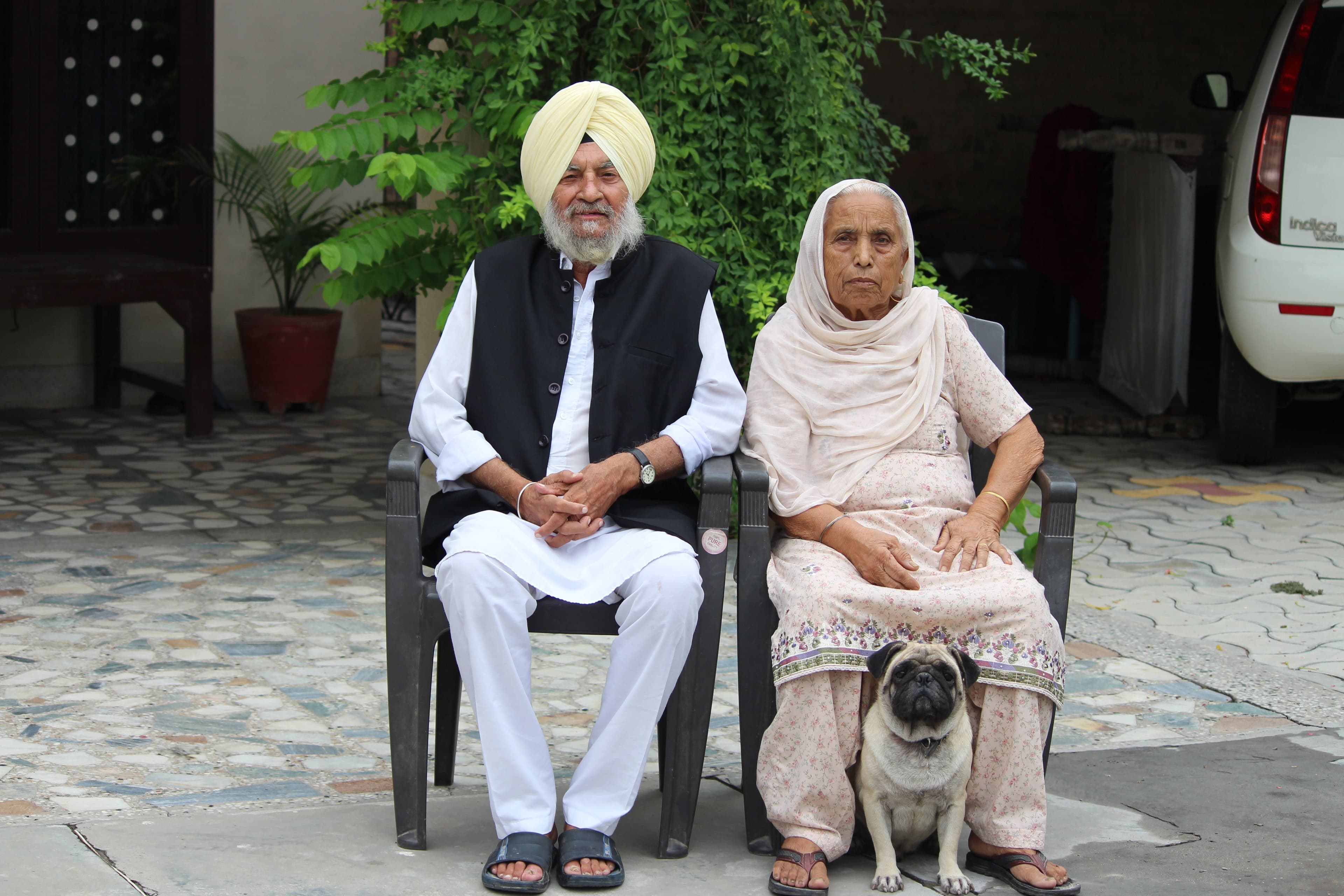An elderly Sikh couple sitting together at home with their pet pug