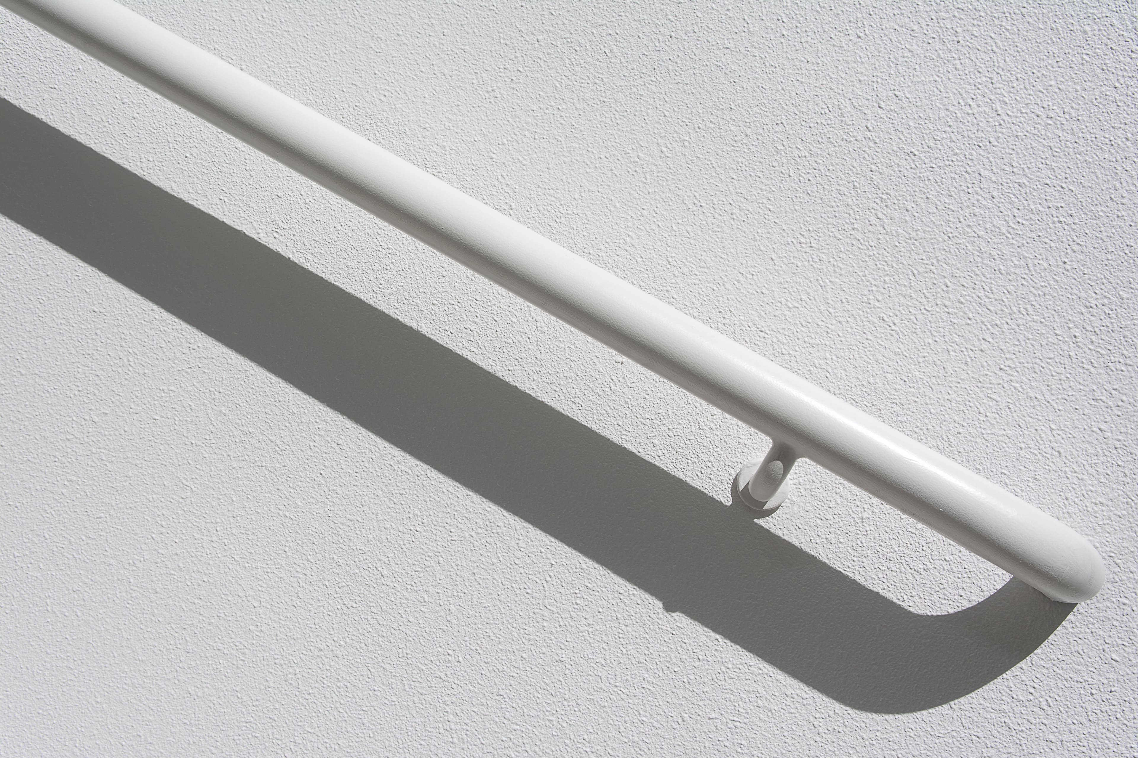 A handrail mounted on a wall, its shadow cast sharply across the paint